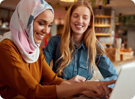 Two women in a coffee shop working together on a laptop